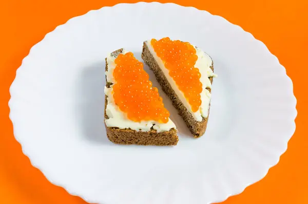 Cut a piece of black rye bread on a white plate, greased with butter and red caviar — Stock Photo, Image