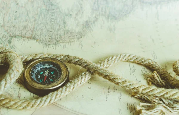 An old vintage compass and a rope on a map with a ray of sun falling on it
