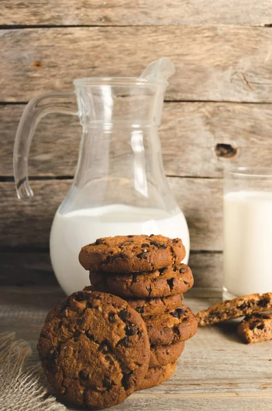 Biscoitos de chocolate de aveia, jarro e copo de leite, fundo de madeira rústico . — Fotografia de Stock