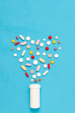 Tabletler ve hap çeşitli. İlaç ve antibiyotik kalp şeklindeki şişe mavi zemin üzerine.