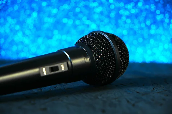 Schwarzes Mikrofon fiel auf den schwarzen Holzboden. Gegen das leuchtend blaue Bokeh.Musikinstrument zum Singen und Karaoke. — Stockfoto