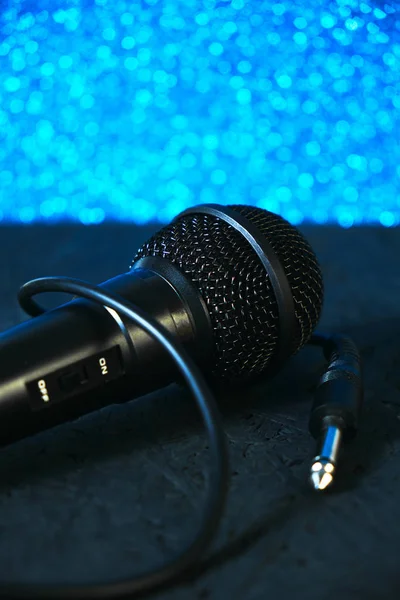 Fekete mikrofon esett a fekete fa padlóra.Against a fényes kék bokeh.Hangszer éneklés és karaoke. — Stock Fotó