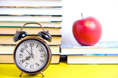 Bir kitabın arka planında eski bir çalar saat ve kırmızı bir elma..