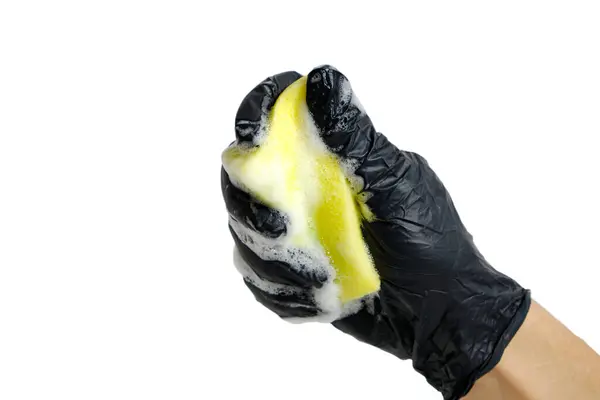 Muž ruka v černé rukavici svírá pěnovou houbu na mytí nádobí s pěnou. — Stock fotografie