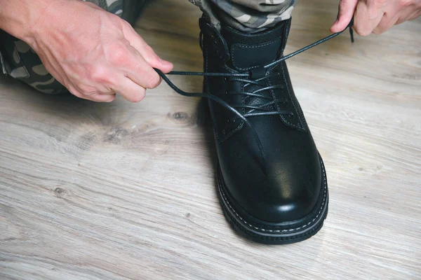 Een man in een militair uniform bindt de veters aan zijn zwarte schoenen. — Stockfoto