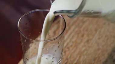 Ev yapımı inek sütü bir testiden bardaklara dökülür. Ahşap bir arka planda..