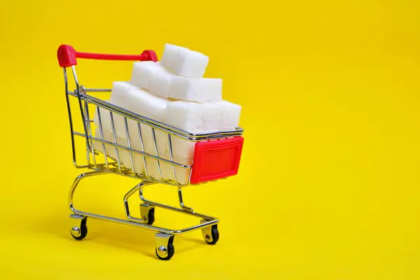 ショッピングカートは黄色の背景に洗練された砂糖キューブで満たされています — ストック写真