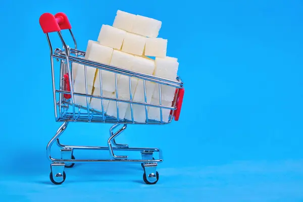ショッピングカートは青の背景に洗練された砂糖キューブで満たされています — ストック写真