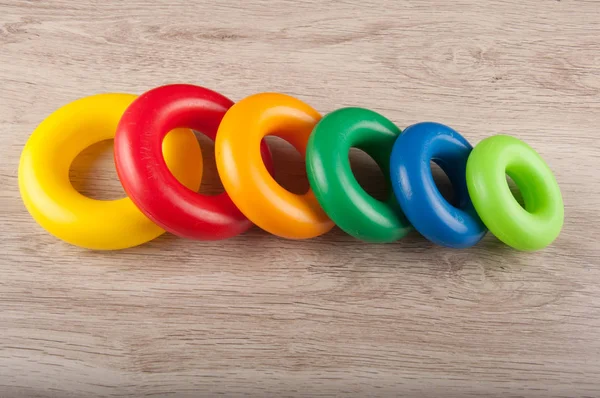 Fila di anelli di plastica multicolore giaceva su sfondo di legno — Foto Stock
