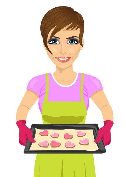 Wanita muda yang memegang baking tray dengan kue berbentuk hati - Stok Vektor