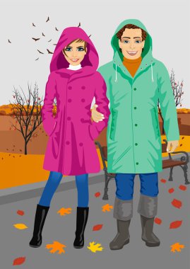 young couple wearing raincoats standing in park in autumn clipart