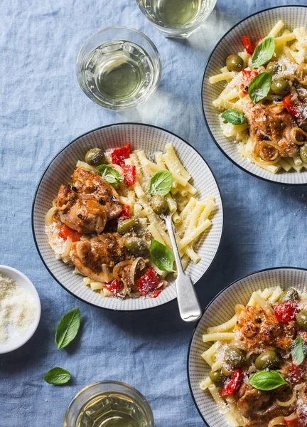 Italian food table. Pasta with slow cooker chicken with olives and sweet peppers, white wine. On a blue background, top view