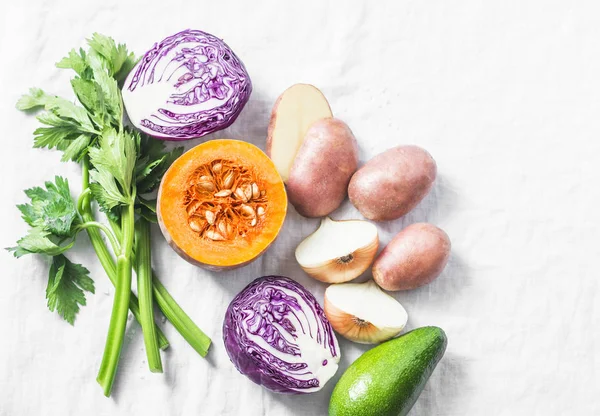 Fresh vegetables - red cabbage, potatoes, onion, celery, pumpkin and avocado on a light background, top view. Clean eating concept