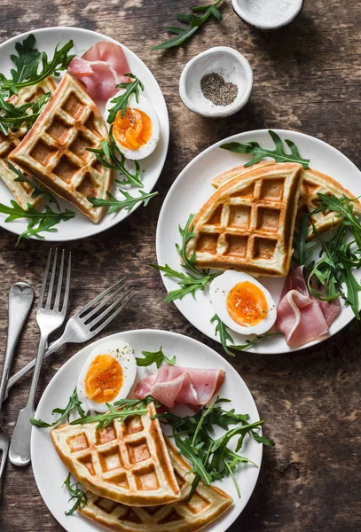 Potato savory waffles with boiled egg, ham and arugula on wooden background, top view. Served breakfast, snack, brunch. Flat lay