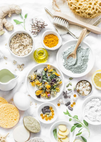 Home beauty products - clay, oatmeal, coconut oil, turmeric, lemon, scrub, dry flowers and herbs, sponges, soap, facial brush on light background, top view. Skin youthfulness, beauty concept. Flat lay — Stock Image Home Beauty Products Clay Oatmeal Coconut Oil Turmeric Lemon Scrub Stock Picture