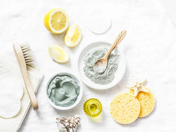 Homemade beauty facial mask. Clay, lemon, oil, facial brush - beauty products ingredients on light background, top view