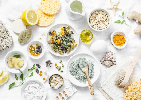 Home beauty products - clay, oatmeal, coconut oil, turmeric, lemon, scrub, dry flowers and herbs, sponges, soap, facial brush on light background, top view. Skin youthfulness, beauty concept. Flat lay — Stock Image Home Beauty Products Clay Oatmeal Coconut Oil Turmeric Lemon Scrub Royalty Free Stock Images