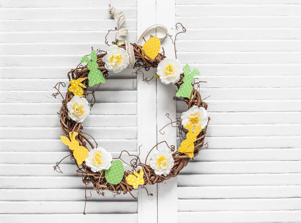 Homemade vine easter wreath with flowers and paper bunnies on a light background. Easter decoration for the house. Creativity concept