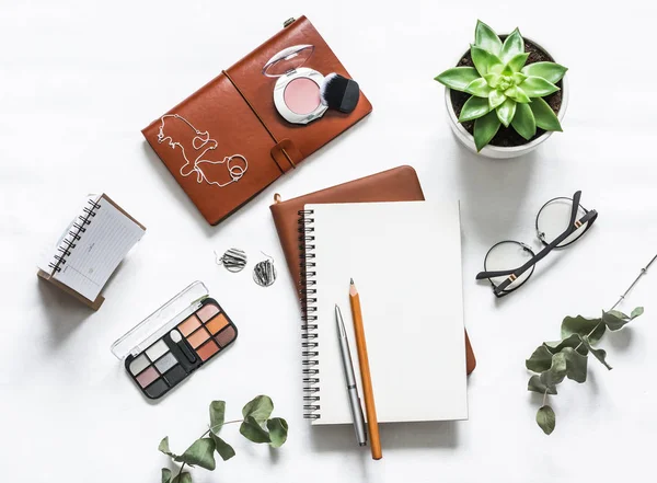 Women\'s table with notebooks, cosmetic, pens, succulent flower on a light table, top view. Flat lay beautiful female still life