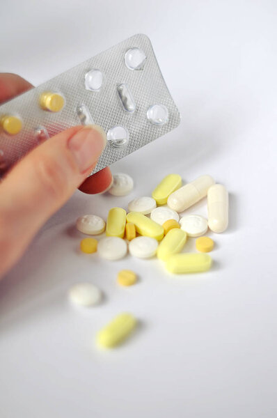 Pharmacy theme. Multicolored Isolated Pills and Capsules on the White Surface. with woman hand holding a blister