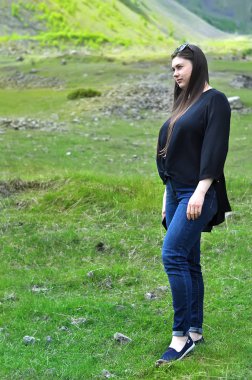 Mavi Jeans güzel kadın dağ yerlere bir genç bahar çimen ile yürüyor.