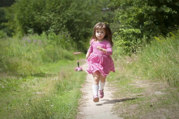 Menina adorável em vestido rosa corre na floresta. Dia ensolarado — Fotografia de Stock