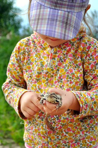 Ein süßes kleines Mädchen hält eine Froschkröte in den Händen und lacht — Stockfoto