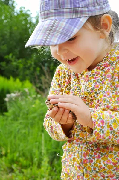 Ein süßes kleines Mädchen hält eine Froschkröte in den Händen und lacht — Stockfoto