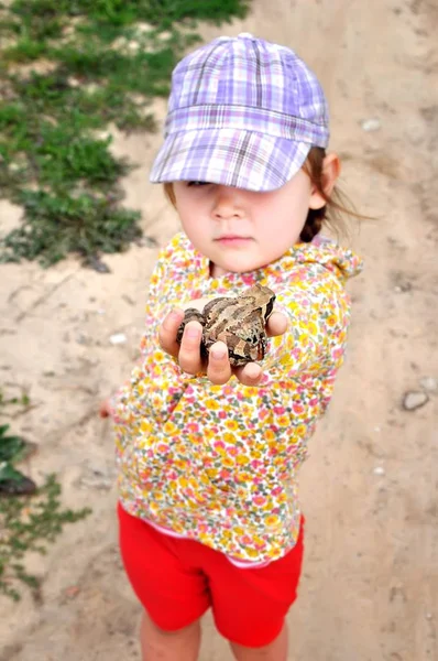 Een schattig jong kind meisje een kikker toad bedrijf in handen en lachen — Stockfoto