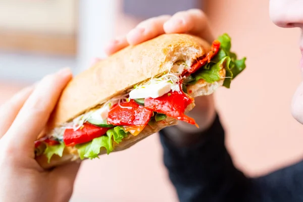 Sebzeli ve peynirli sandviç yiyen kadın.