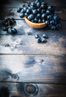 Tahta bir arka planda bambu kasesinde bir demet siyah üzüm.