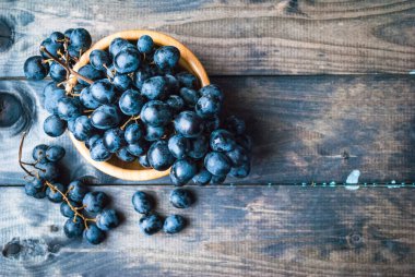 Tahta arka planda bambu kasesinde bir demet siyah üzüm. Boşluğu kopyala