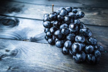 Mavi ahşap arka planda bir demet siyah üzüm.