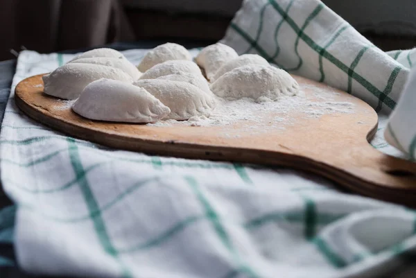 Raw dumplings sprinkled with flour on a kitchen board and a striped towel — ストック写真