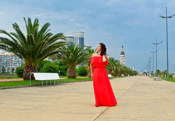 Девушка позирует в длинном красном платье на набережной — стоковое фото