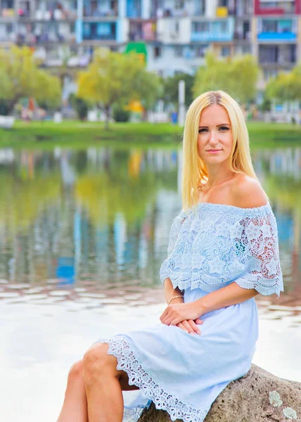 Hermosa chica en un vestido azul sentado junto al lago . — Foto de Stock