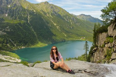 Morskie Oko Gölü yakınlarındaki dağlarda yaşayan bir turist kadın. Kayalıklarda otururken. Yüksek dağlarda maceralar. Tatra Ulusal Parkı 'nda yürüyüş yapan kız, Zakopane, Polonya. Arkaplanda Karpat Dağları.