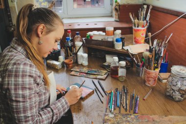 Kız ressam stüdyoda resim yapıyor. Aziz Niklas ikonunun kopyası. Stüdyodaki sanatçının çalışmaları. Arkaplan sanat işyerindeki fırçalar ve boyalar.