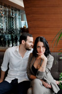 İş aşkı. Modaya uygun yetişkin bir çift. Beyaz gömlekli bir adam ve kahverengi elbiseli bir kadın. Kanepede oturuyorlar..