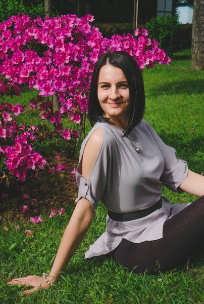 Güzel esmer kadın parkta pembe çiçeklerin yanında çimlerin üzerinde oturuyor. Gülümse, Batumi, Georgia 'daki tatlı kız. Yaz zamanı..