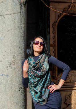 Moda, sokakta elbise ve atkı takan esmer kadın. Güneşli bir bahar gününün tadını çıkarıyor. Georgia, Batumi 'de poz veren kız model. Arka planda eski şehir.