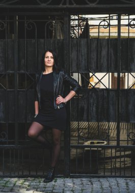 Şehirde poz veren deri ceketli, pozitif gülüşlü esmer hippi kadın. Georgia, Batumi 'deki kız model. Kapılar arka planda.