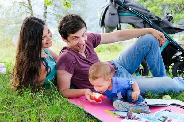 Little boy eats an apple from his father's hands on outdoor picnic time. Lifestyle. Sincere moments of happy family. Leisure, childhood, parenthood and enjoying life together concept.