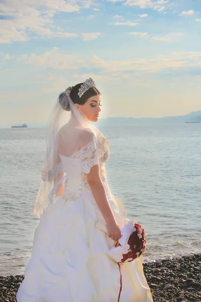Wedding by the sea. Smilling bride with a red bouquet. Mountains and sea background. Adorable caucasian bride. Sunrise view. Concept marriage, just married