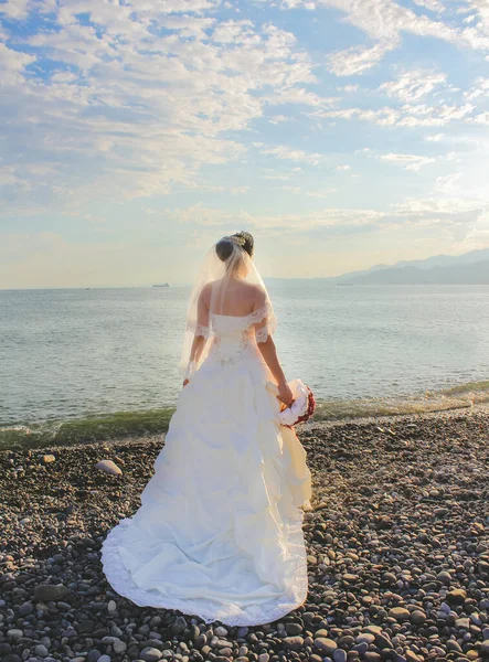 Wedding by the sea. Beautiful bride with a red bouquet. Mountains and sea background. Bride looking at sunrise. Back view. Concept marriage, just married