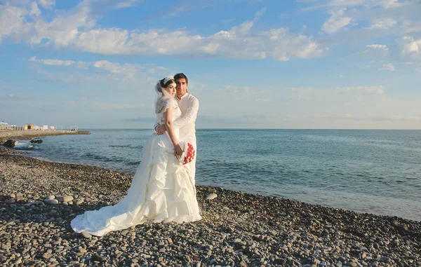 Deniz kenarında düğün. Güzel bir çift yeni evli. Gelinliği suda kırmızı buketli gelin. Gelin ve damat gün doğumuna bakıyor. Batumi, Georgia 'da yeni evlenmiş..