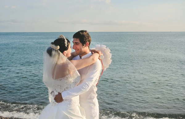 Wedding by the sea. Beautiful couple of newlyweds. Bride with a red bouquet in a wedding dress at the water. Bride and groom looking to each other. Just married in Batumi, Georgia.