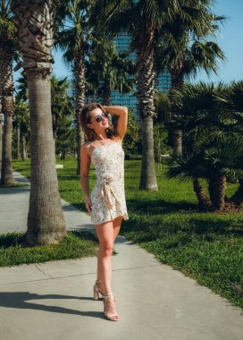 Palmiye ağacının yanındaki plajda güneş gözlüklü seksi fitness kadını. Çekici kız dinleniyor, yaz cennetinin tadını çıkar..