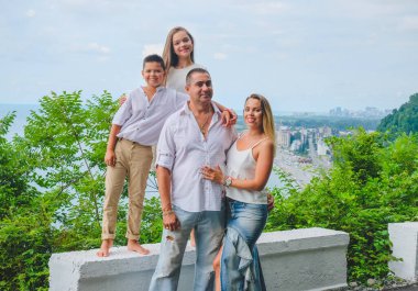 Neşeli, mutlu aile, baba, anne, oğul ve kız deniz kenarında yürüyüş yapmaktan zevk alıyorlar. Yürüme yolunda çıplak ayaklı beyaz elbiseli bir aile. Yeşil orman arka planı.