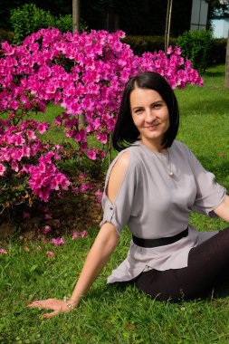 Güzel esmer kadın parkta pembe çiçeklerin yanında çimlerin üzerinde oturuyor. Gülümse, Batumi, Georgia 'daki tatlı kız. Yaz zamanı..